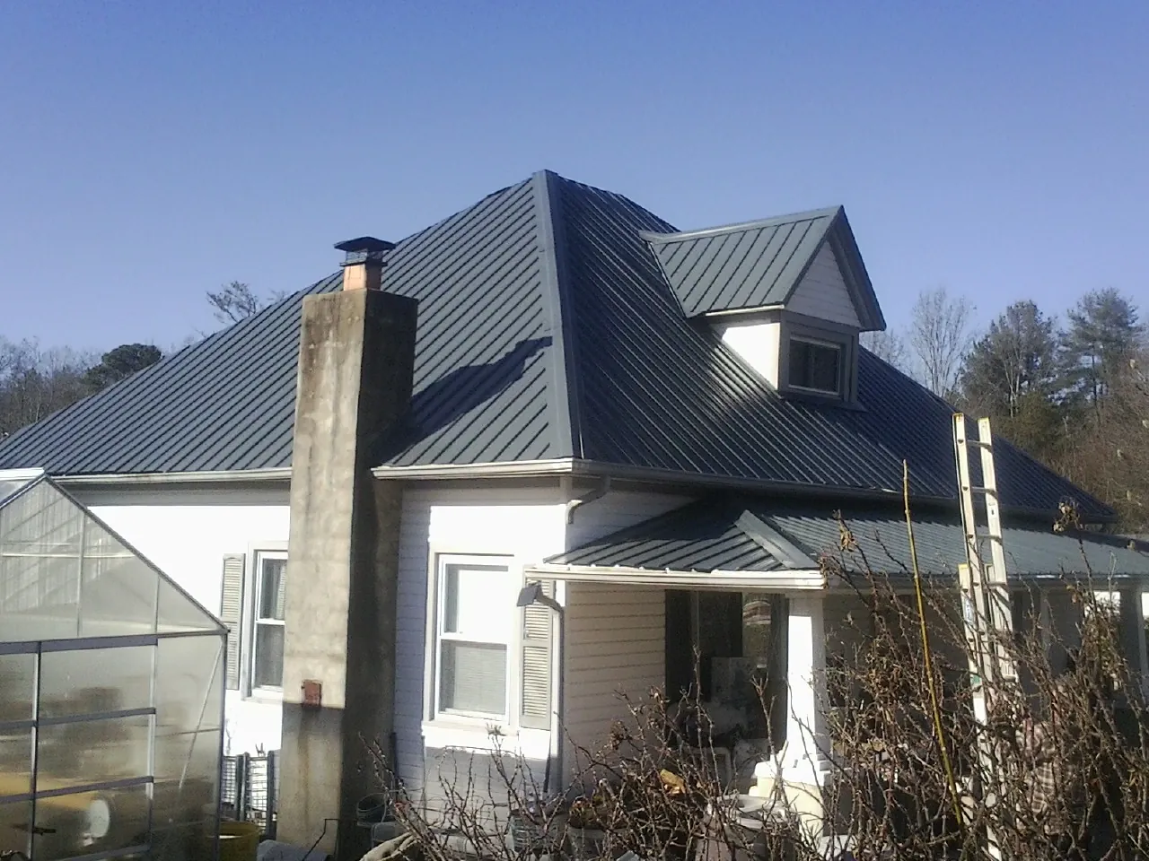 Dark blue standing seam metal roof on a white farmhouse with dormer — Slate & Tile Roof Repair by Roofing Brothers in Madison Lake