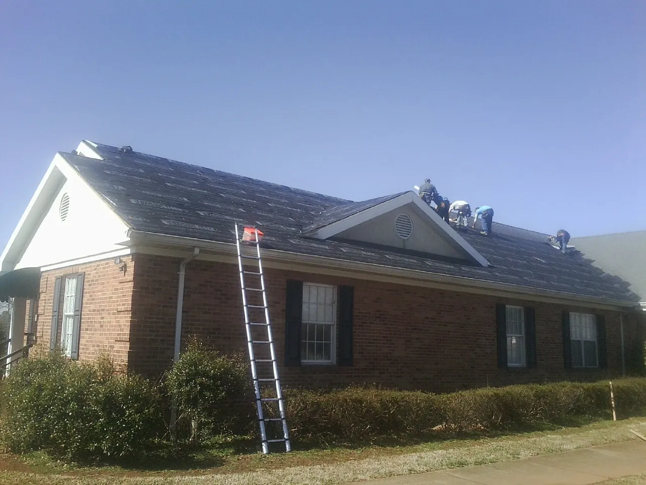 Crew tearing shingles off a brick ranch roof with a ladder set — Emergency Roof Repair work by our crew in Madison Lake
