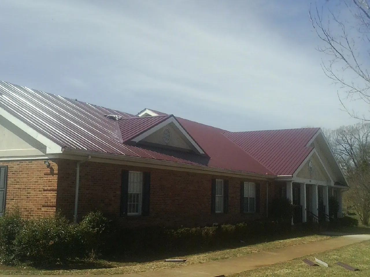 Red metal roof with gabled entries on a long brick building, from a Hail Damage Roof Repair job in Madison Lake
