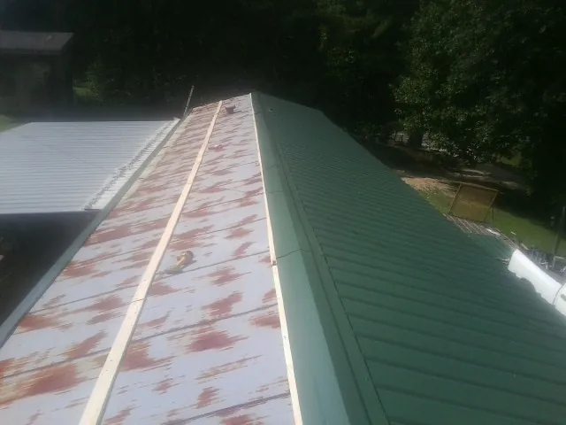 Old rusted panels beside newly installed green metal roofing — Wind Damage Roof Repair by Roofing Brothers in Madison Lake