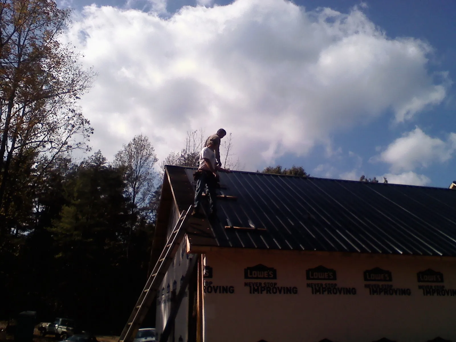 Roofer fastening dark metal panels high against a cloudy sky, from a Roof Inspection job in Madison Lake