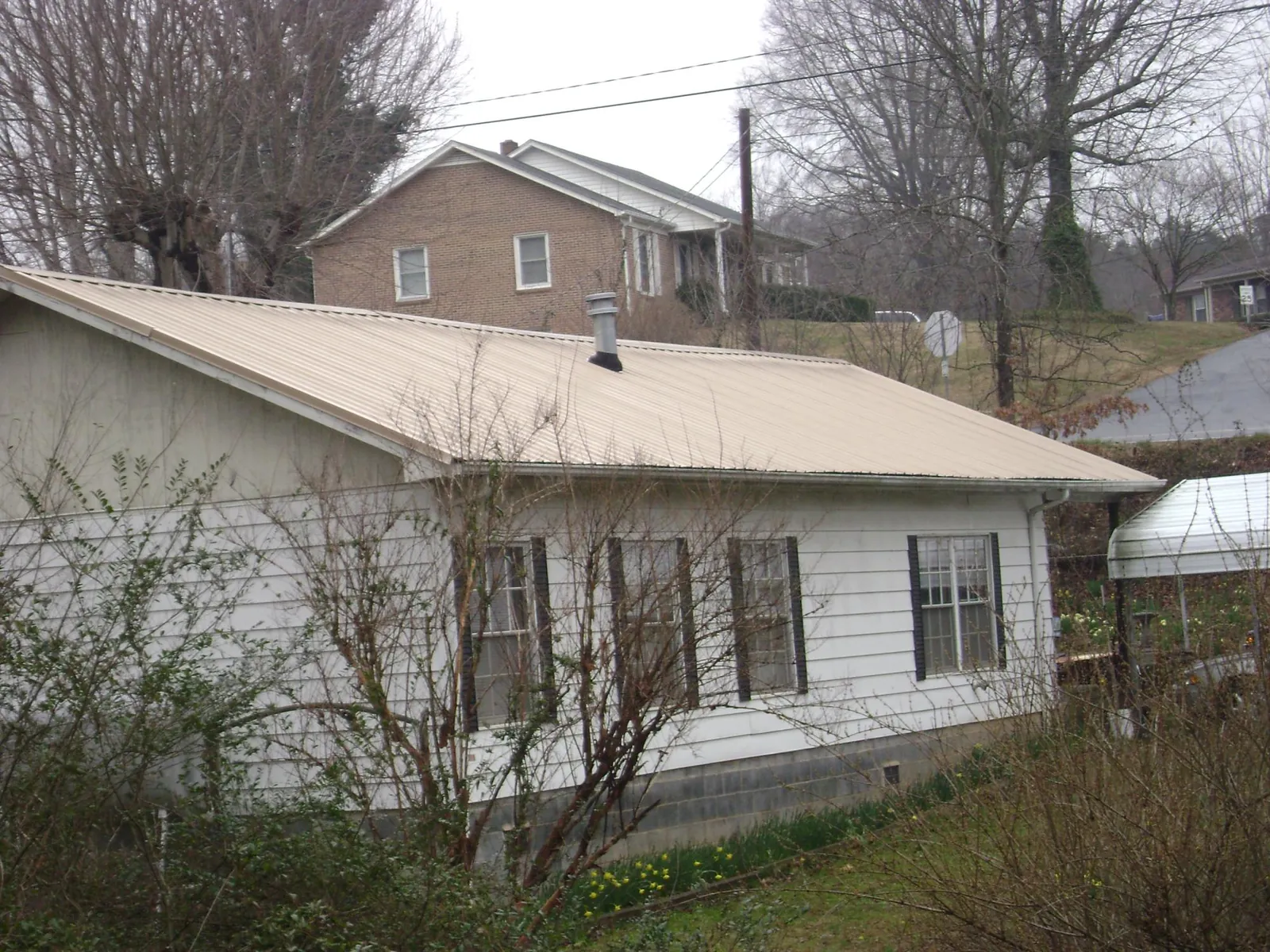 Tan metal roof on a white sided house set into a hillside — Commercial Roofing by Roofing Brothers in Madison Lake