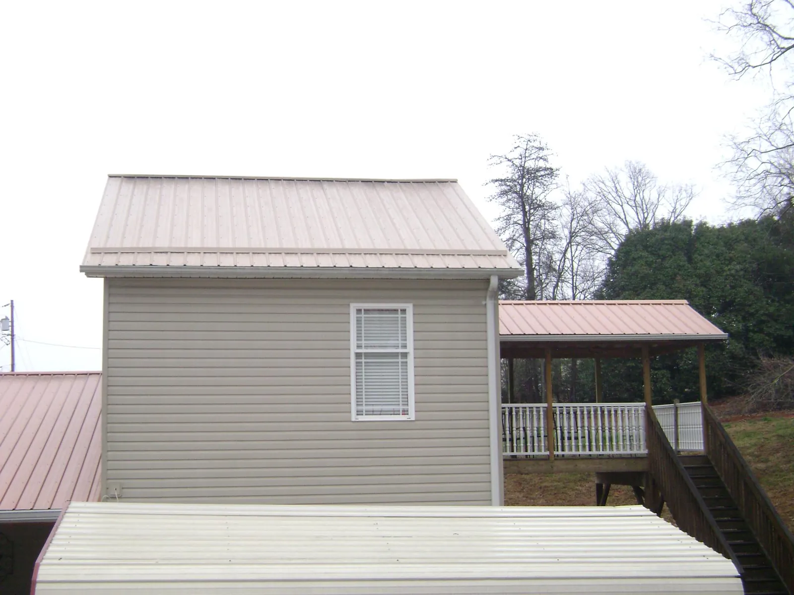 Tan metal roofs on a two story addition and attached porch, from a Roof Replacement job in Madison Lake
